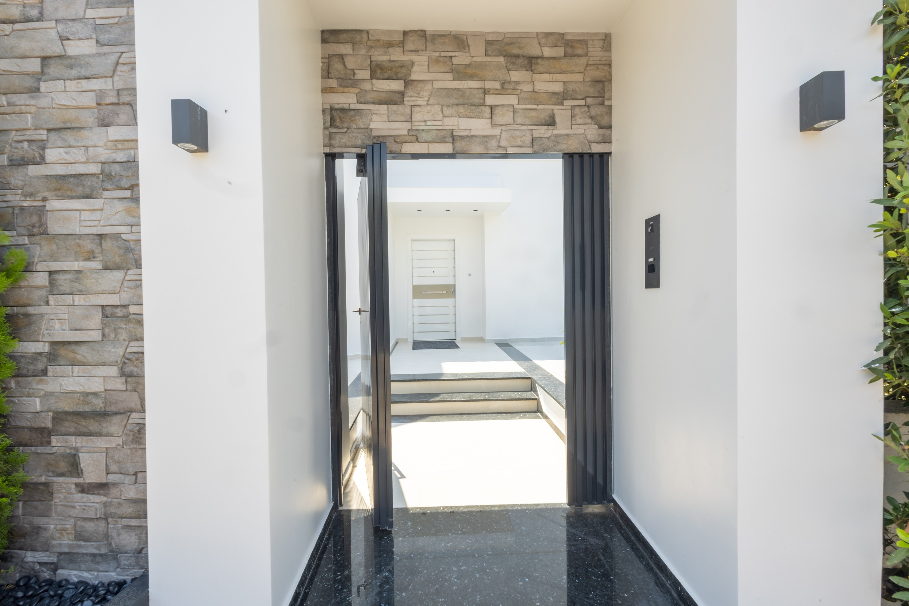 Stone-clad garden passage framing the villa's white entrance court
