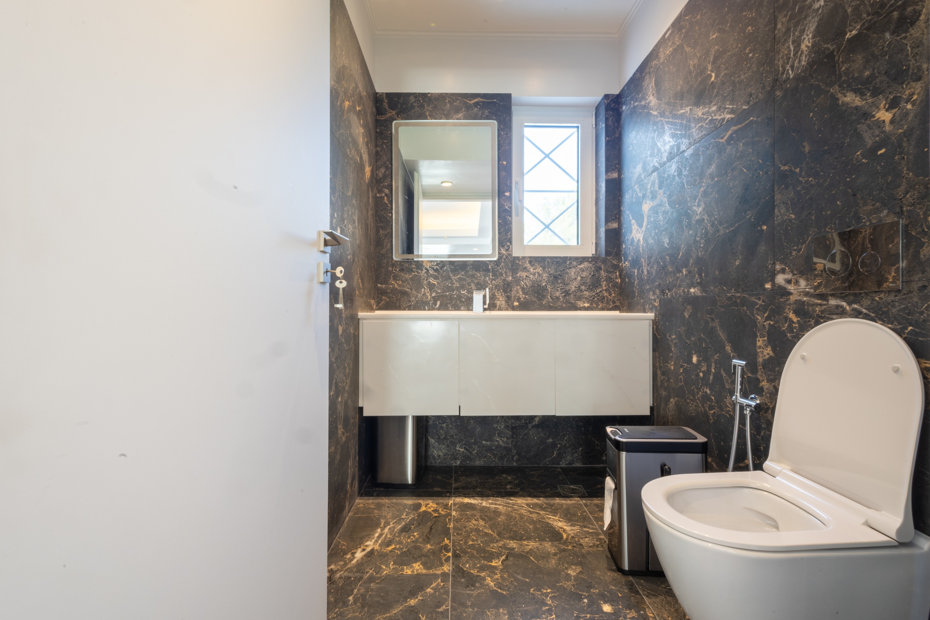 Guest powder room with dark veined marble, a luminous vanity and inset mirror