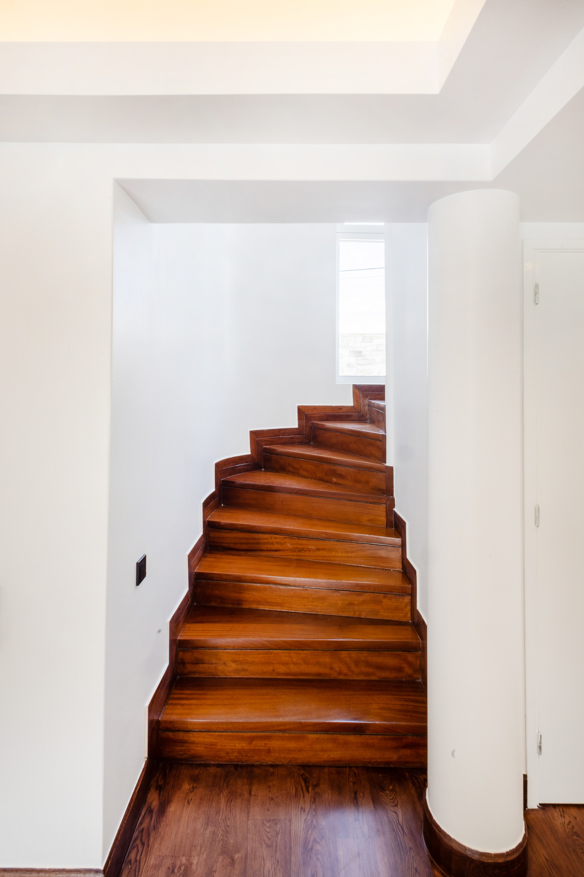 Broad curved timber staircase rising around a white column